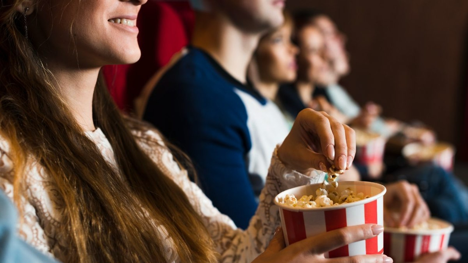Mulher sorridente segura balde de pipoca em cinema, com outros espectadores assistindo ao fundo