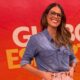 Joanna de Assis sorri com óculos, camisa jeans, em fundo vermelho com texto 'Globo Esporte'
