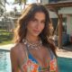 Bianca Andrade sorrindo em biquíni azul com colar, piscina e palmeiras ao fundo