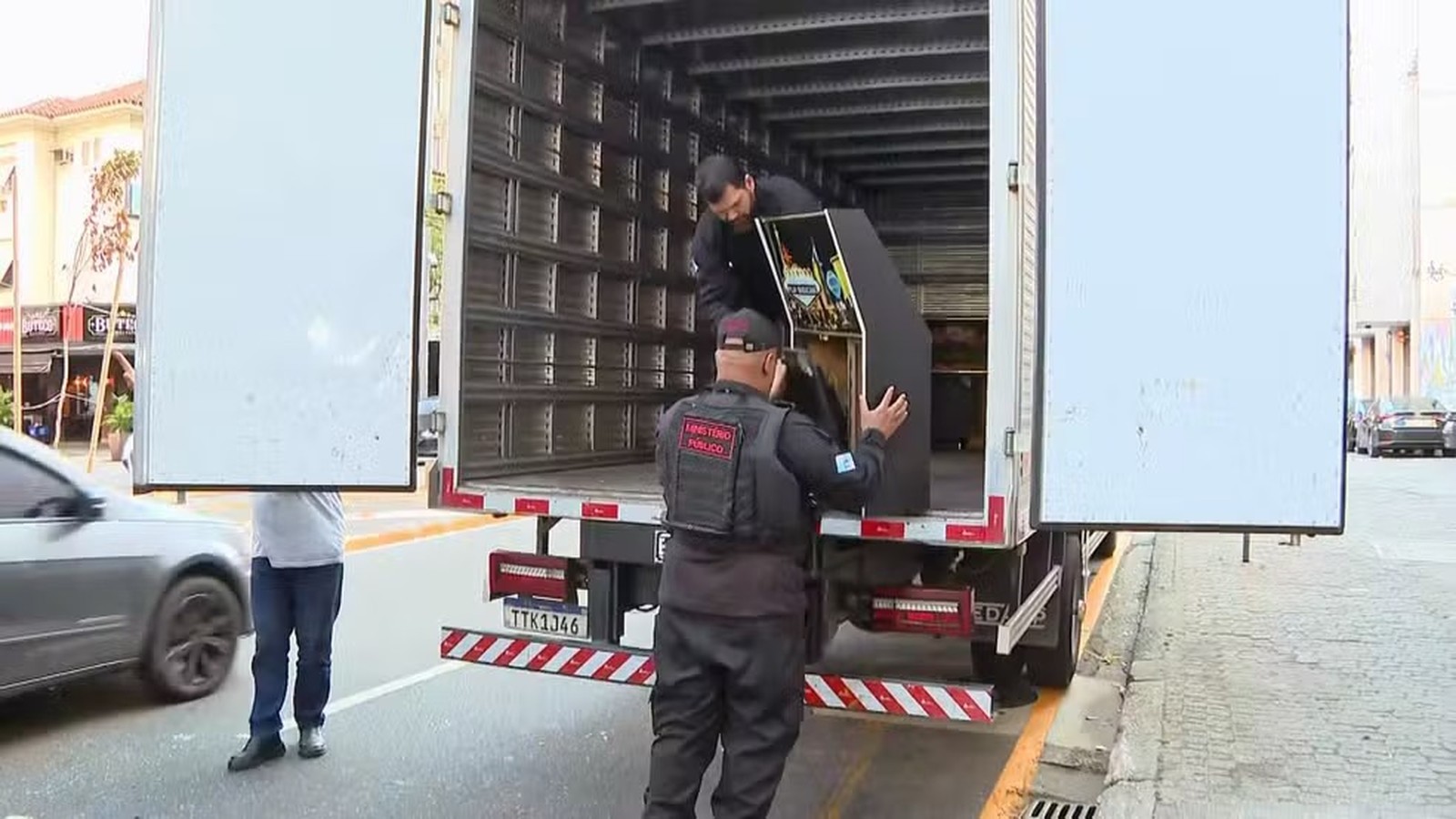 Agentes do Ministério Público carregam máquina caça-níqueis em caminhão de apreensão na rua