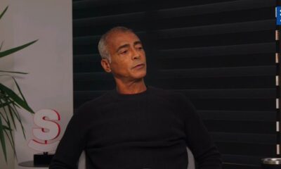 Romário, cabelo grisalho, camisa escura, sentado, olhando para a direita em ambiente interno