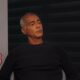 Romário, cabelo grisalho, camisa escura, sentado, olhando para a direita em ambiente interno