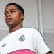 Jovem de pele escura com camisa branca do Real Madrid e Adidas olhando para o lado