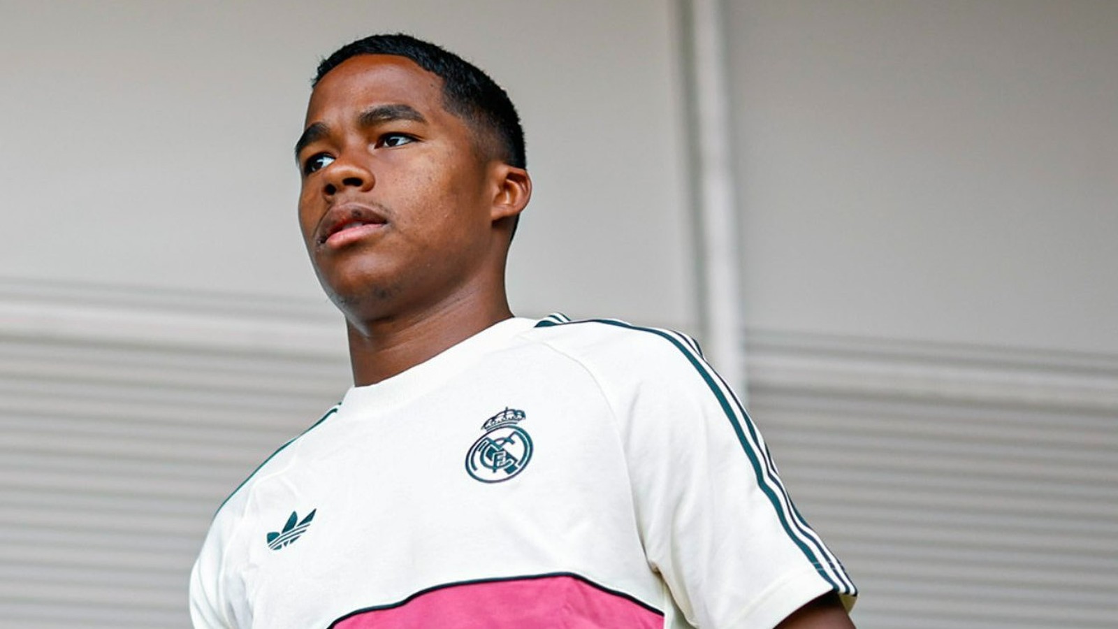 Jovem de pele escura com camisa branca do Real Madrid e Adidas olhando para o lado