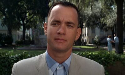 Tom Hanks como Forrest Gump, em terno claro, com expressão séria em parque
