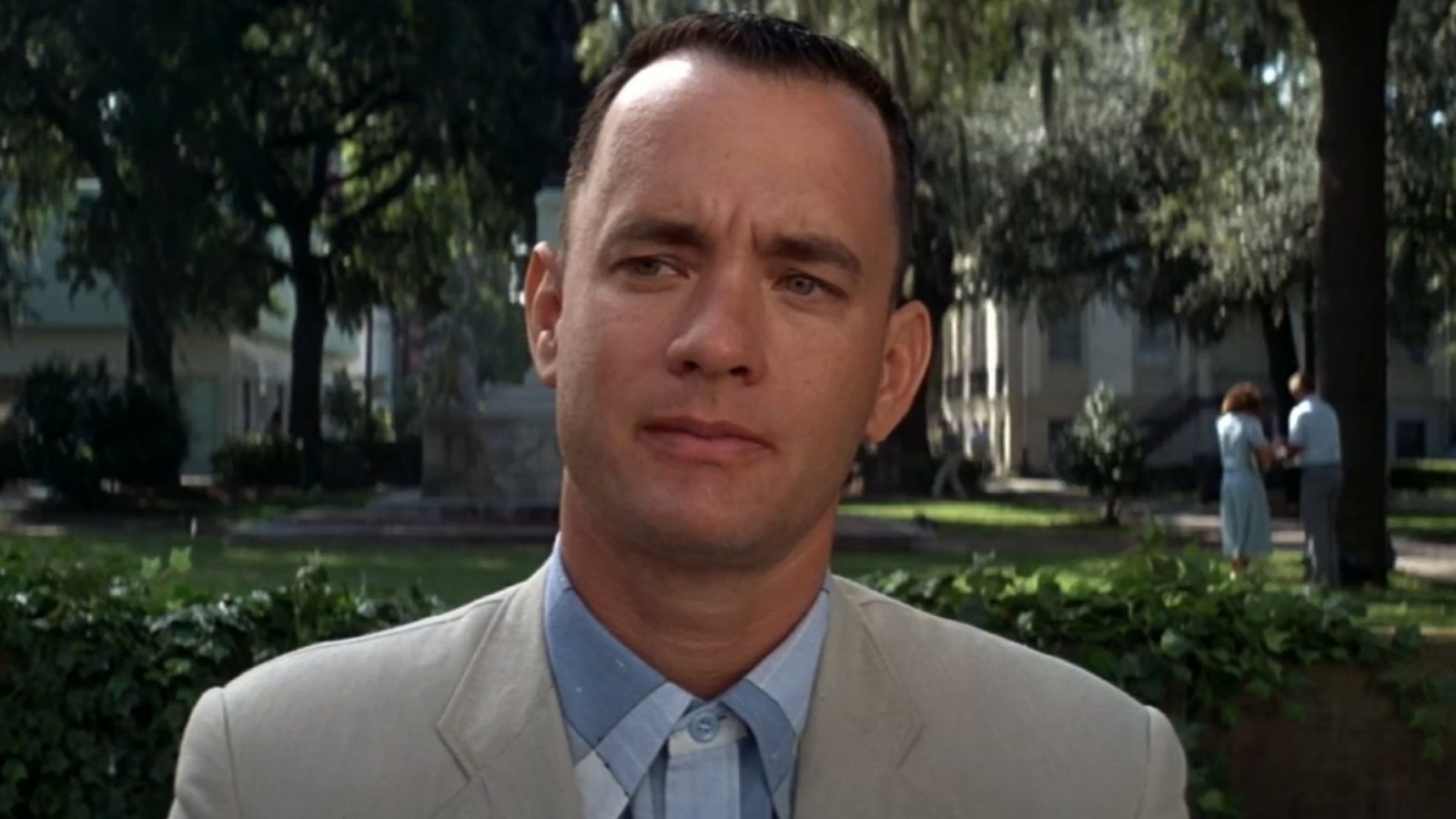 Tom Hanks como Forrest Gump, em terno claro, com expressão séria em parque