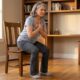 Adulto acima de 50 anos se levantando de uma cadeira firme sem apoiar as mãos, com os pés no chão e postura controlada.