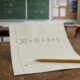 Folha sobre uma mesa de estudos com a expressão “30 + 15 ÷ 3 × 5” escrita em destaque e um lápis ao lado, sem apresentar a resposta