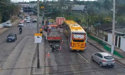 Ônibus amarelo, caminhão de bombeiros vermelho e moto caída no asfalto com cones de trânsito