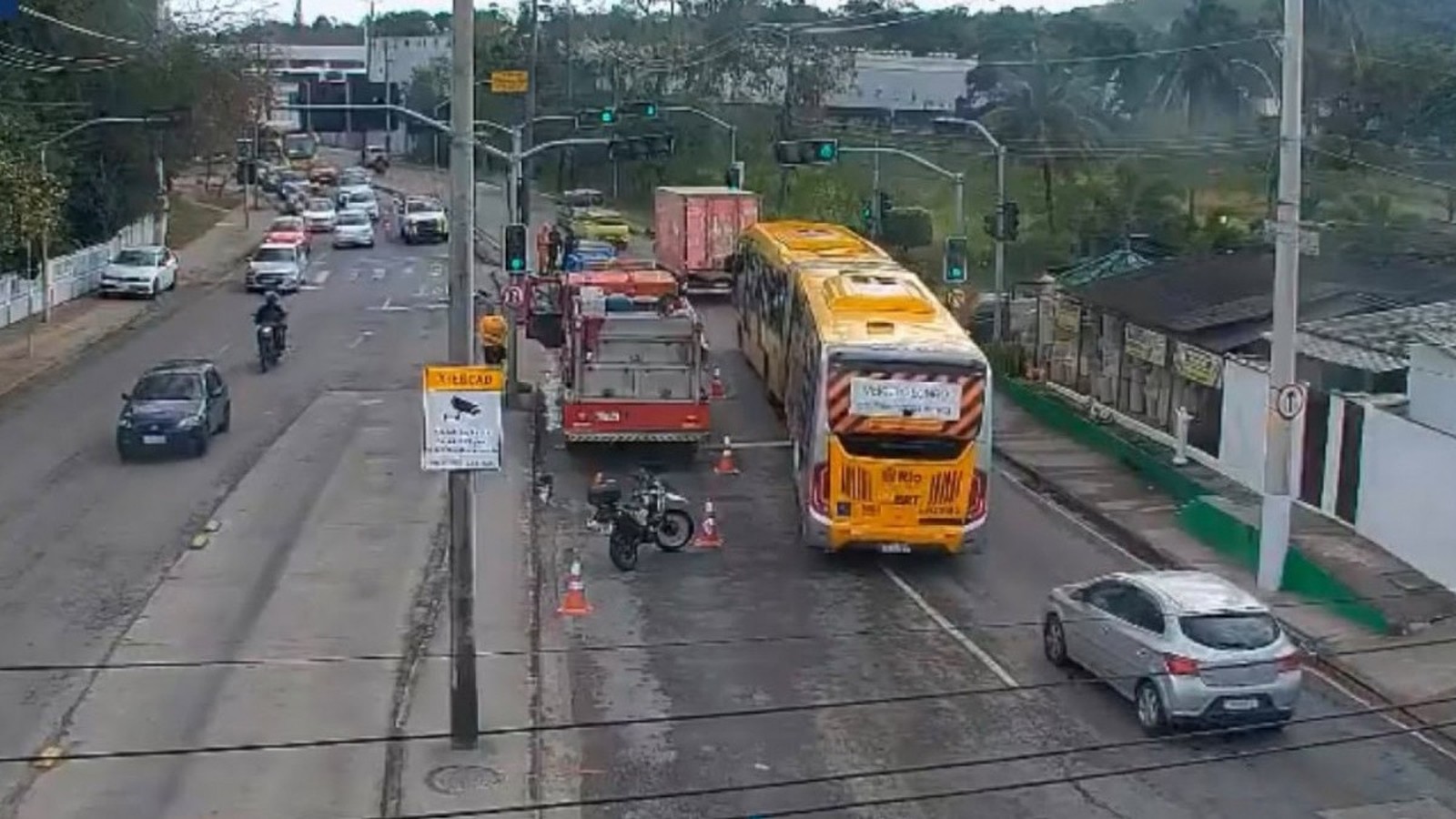 Ônibus amarelo, caminhão de bombeiros vermelho e moto caída no asfalto com cones de trânsito