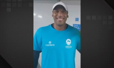 Professor Carlos Eduardo Cerqueira sorri com camiseta azul Maniacs World Cup e boné branco