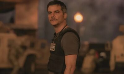 Wagner Moura com bigode e colete de imprensa 'PRESS' em ambiente de combate
