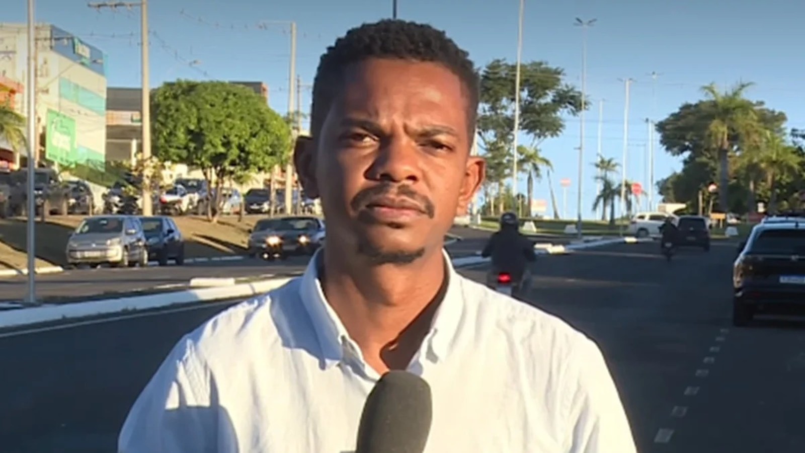 Repórter Kelven Melo com microfone em rua movimentada, com carros e prédios ao fundo