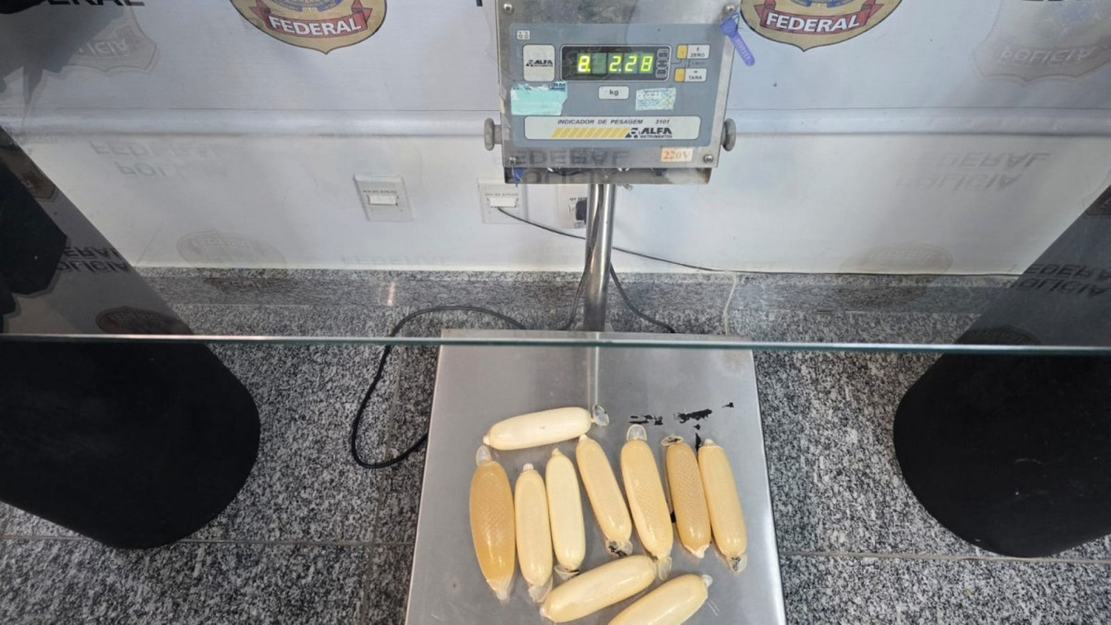 Pacotes de cocaína líquida em preservativos sobre balança digital marcando 2.28 kg e logo PF