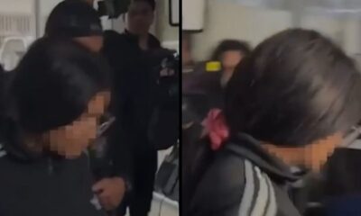 Mulher de cabelo escuro, rosto borrado, blusa preta com listras brancas, rosa na cabeça