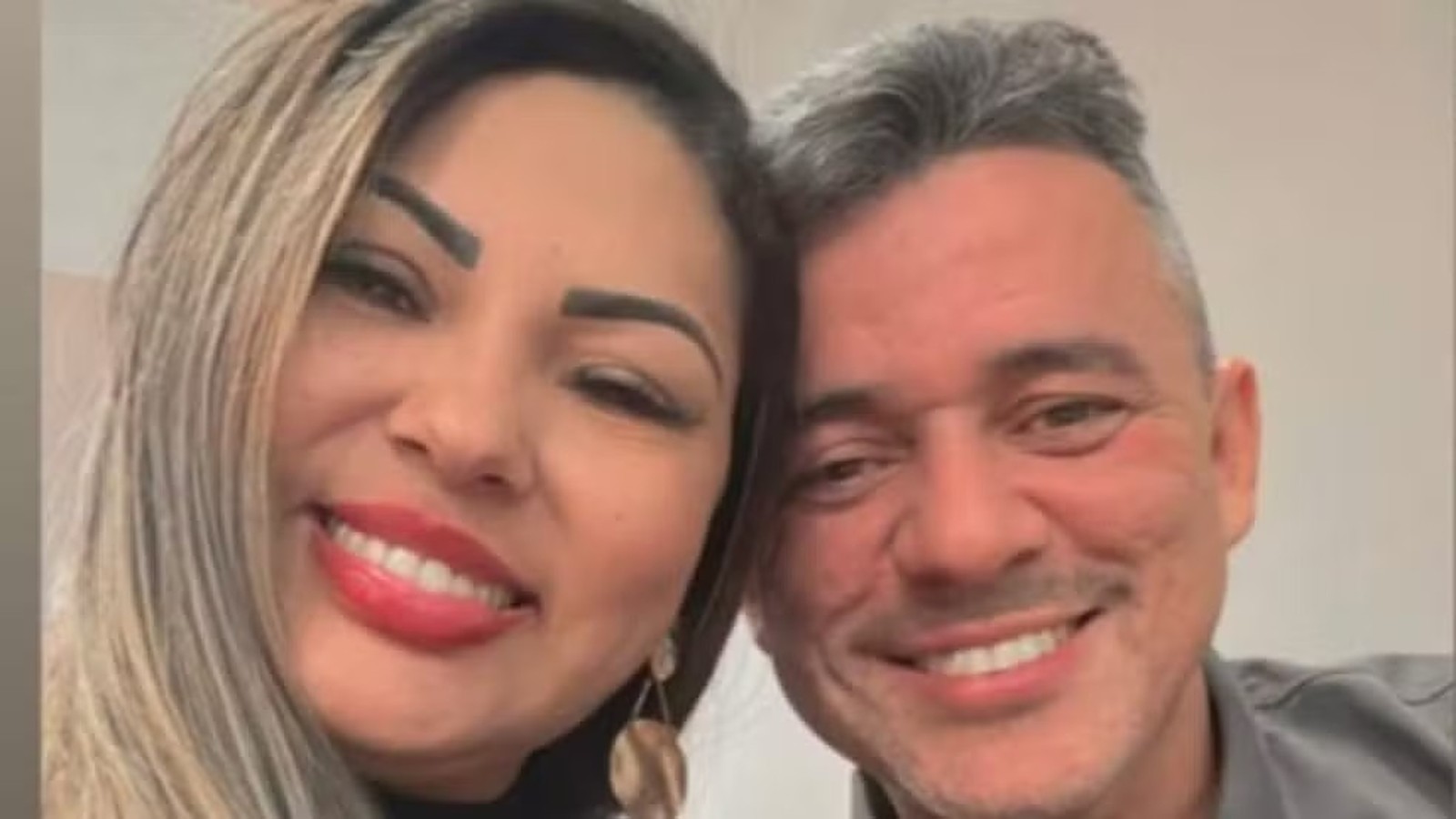 Selfie de uma mulher sorridente com batom vermelho ao lado de um homem sorrindo