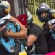 Mulher de capacete segurando cão preto com capacete amarelo e colete em moto