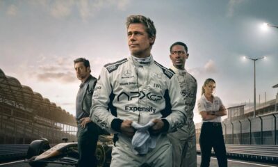Atores Brad Pitt e Damson Idris em macacões de piloto APX GP na pista, com carro de F1 e equipe