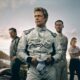 Atores Brad Pitt e Damson Idris em macacões de piloto APX GP na pista, com carro de F1 e equipe