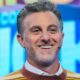 Luciano Huck sorrindo, com cabelo grisalho, barba e suéter listrado marrom e amarelo