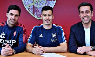 Mikel Arteta, Gabriel Martinelli e Edu Gaspar sorrindo enquanto Martinelli assina contrato pelo Arsenal