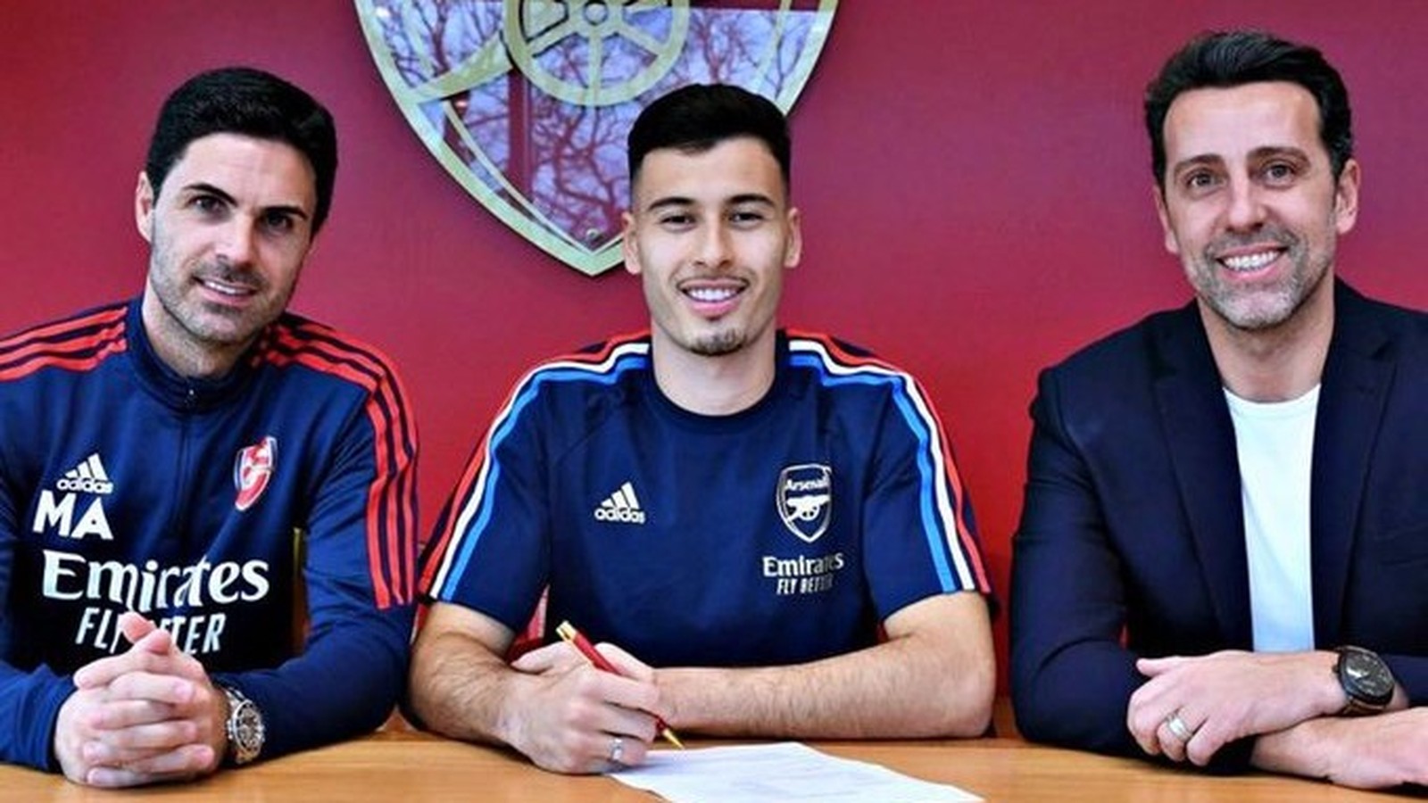 Mikel Arteta, Gabriel Martinelli e Edu Gaspar sorrindo enquanto Martinelli assina contrato pelo Arsenal