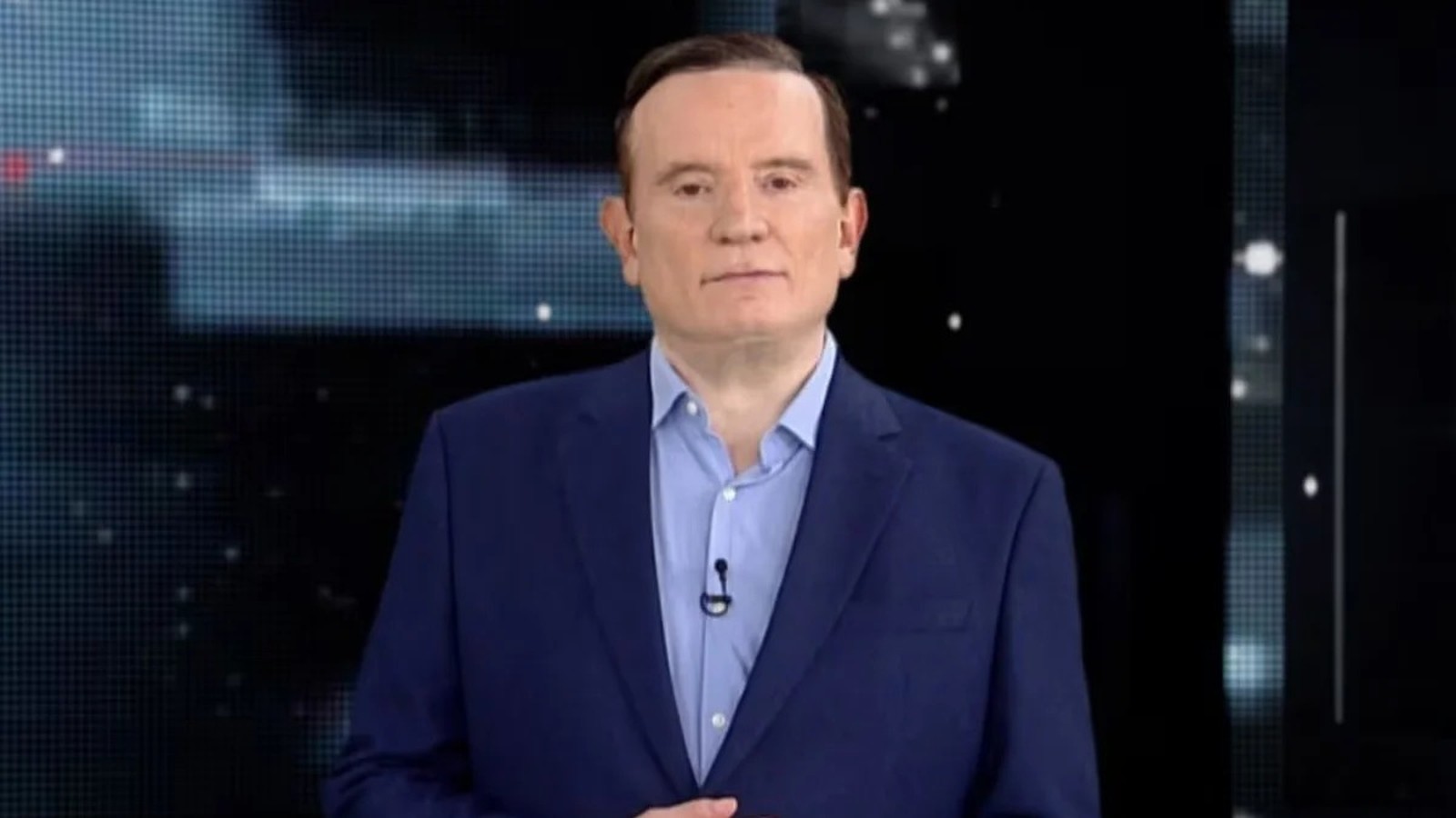 Jornalista Roberto Cabrini de terno azul e camisa em estúdio, olhando para frente