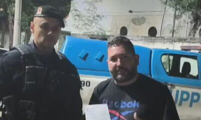 Policial fardado e homem com camiseta Reebok posam à frente de viatura UPP