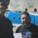 Policial fardado e homem com camiseta Reebok posam à frente de viatura UPP