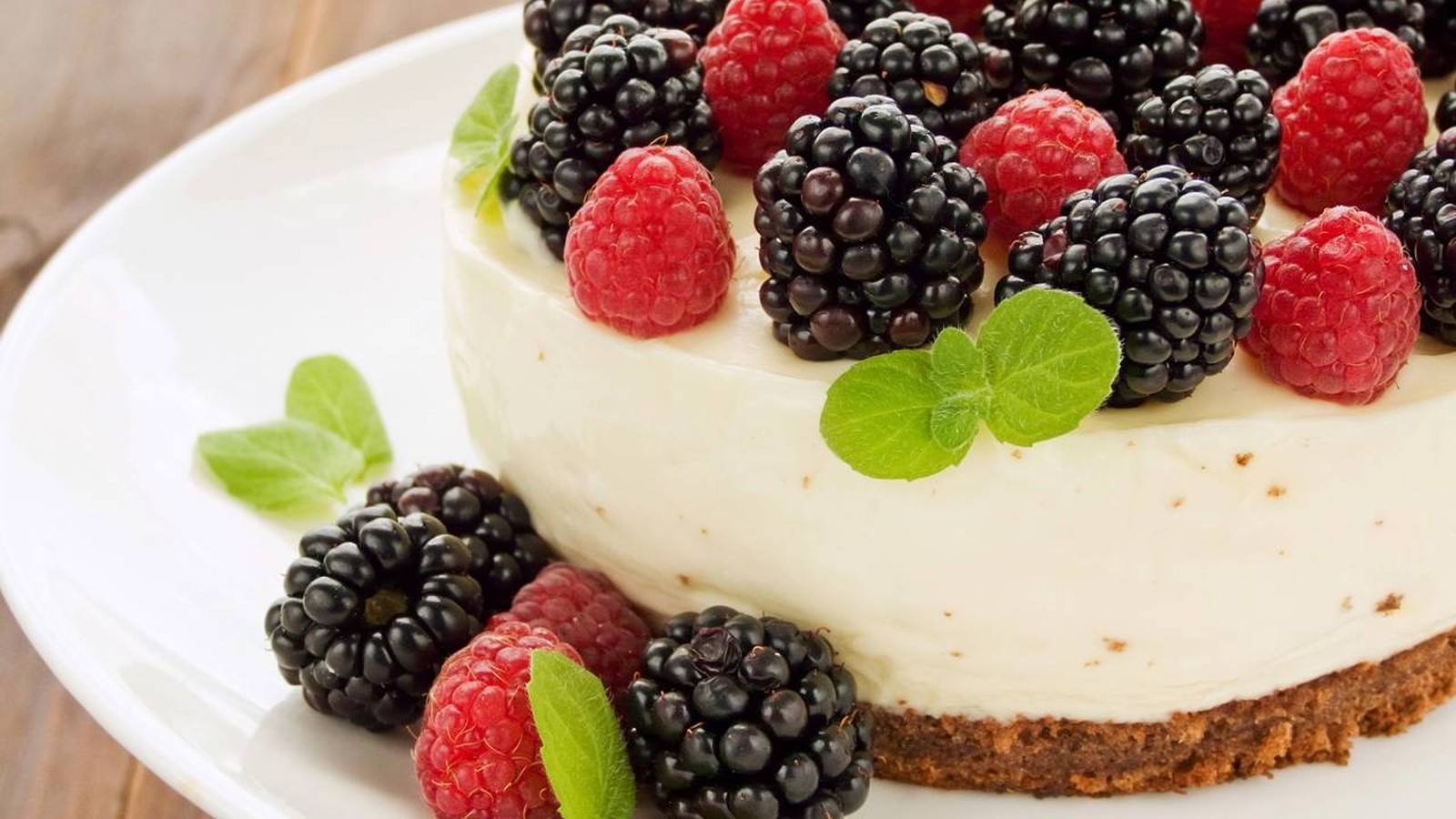 Cheesecake cremoso com amoras, framboesas e folhas de hortelã em um prato branco