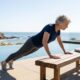 Mulher de 60 anos fazendo flexão inclinada em um banco firme ao lado de uma piscina, durante férias em Malibu