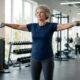 Mulher de 70 anos fazendo desenvolvimento de ombros com halteres leves em uma academia