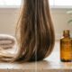 Mecha de cabelo castanho com pontas alinhadas e brilhantes ao lado de um frasco de óleo de argan