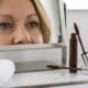 Máscara de cílios marrom aberta ao lado de um espelho que reflete olhos maduros com cílios definidos e maquiagem leve