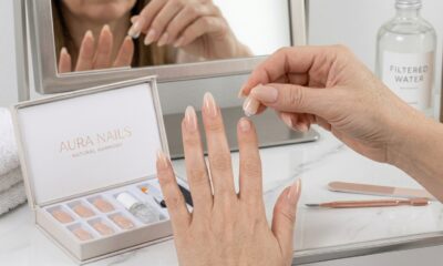 Mão feminina com unhas postiças press-on longas e naturais, com uma peça sendo aplicada em casa