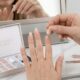 Mão feminina com unhas postiças press-on longas e naturais, com uma peça sendo aplicada em casa