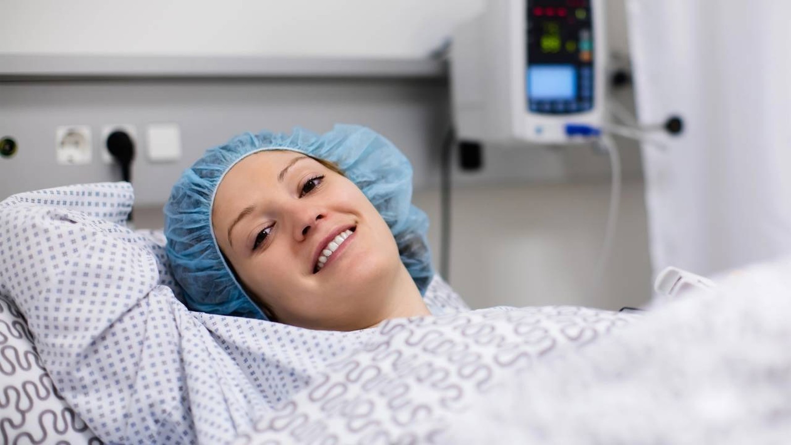 Paciente sorrindo de touca e avental cirúrgico na cama de um hospital