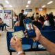 Pessoa usa celular com reconhecimento facial Gov.br e segura documento de identidade em sala de espera