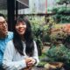 Homem e mulher asiáticos sorrindo em abraço, em frente a um jardim japonês com lanterna de pedra
