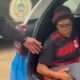 Mulher de óculos e gorro sentada no porta-malas de uma viatura policial