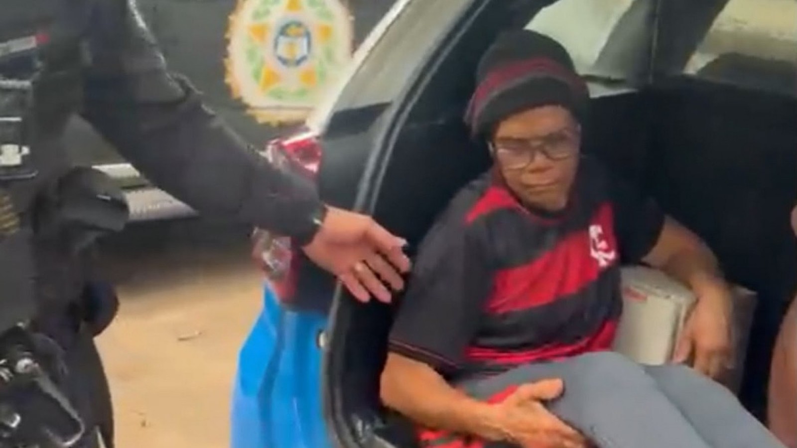Mulher de óculos e gorro sentada no porta-malas de uma viatura policial