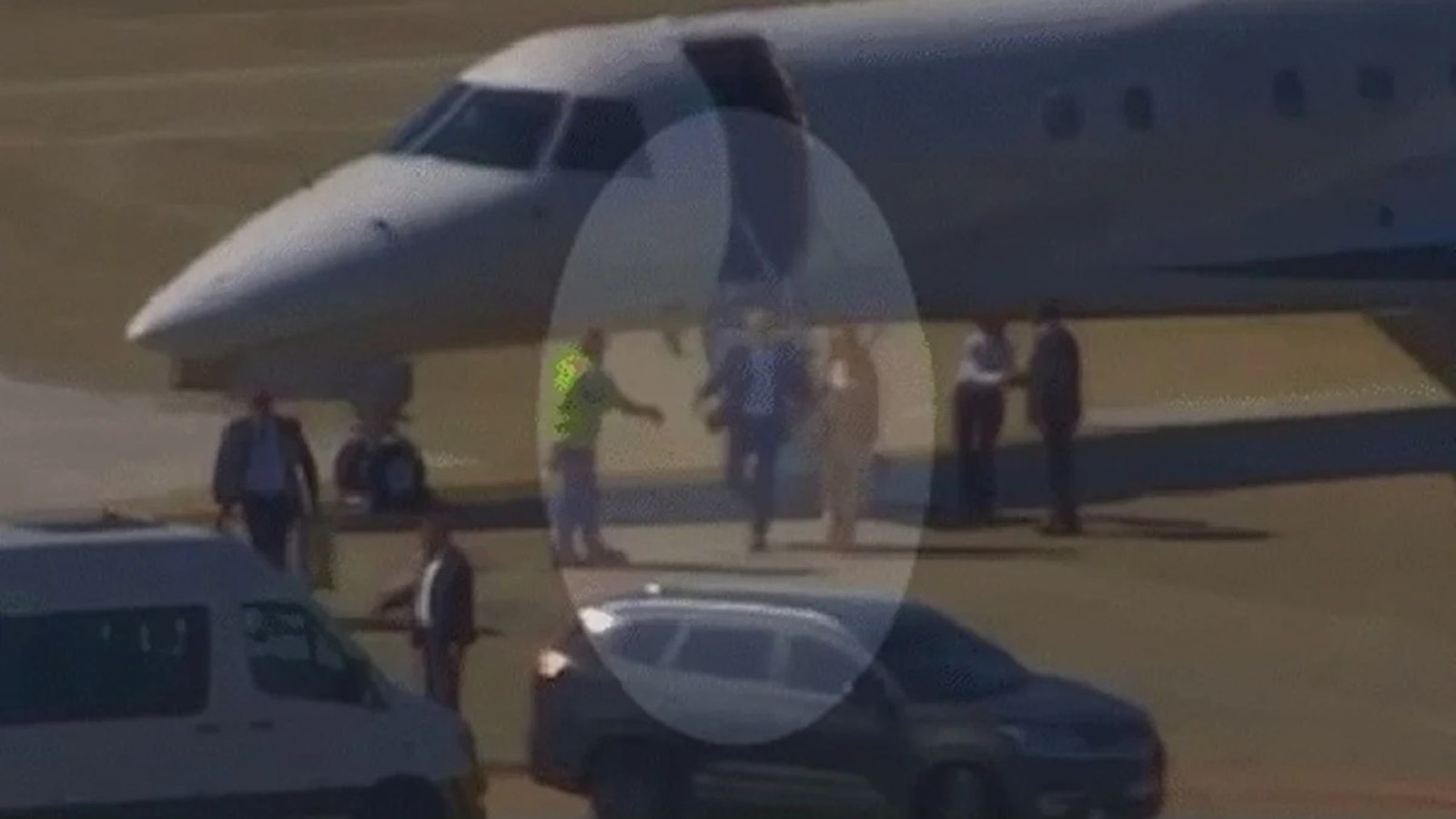 Pessoas descendo de jatinho branco em aeroporto, com van e SUV por perto