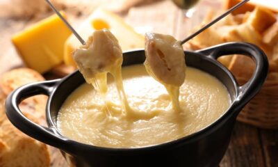 Pedaços de pão com queijo derretido escorrendo de garfos em panela de fondue