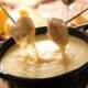 Pedaços de pão com queijo derretido escorrendo de garfos em panela de fondue
