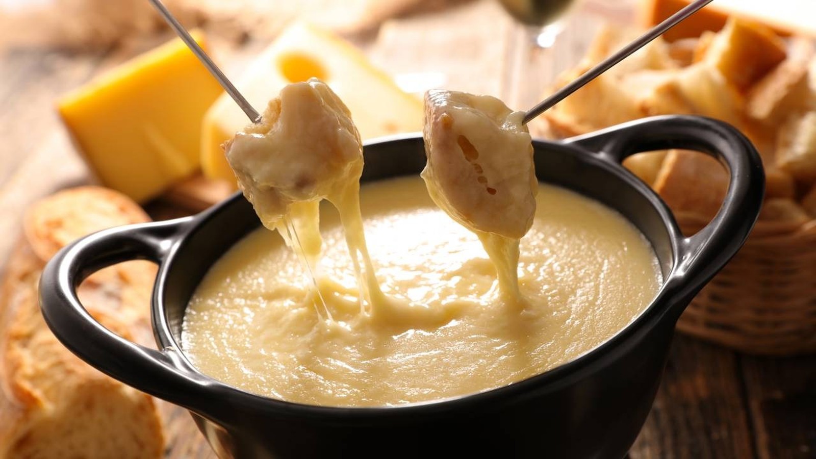 Pedaços de pão com queijo derretido escorrendo de garfos em panela de fondue