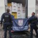 Dois policiais seguram bandeira da PMERJ; atrás, caminhão com caixas Kerfrango e viatura policial