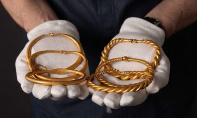 Mãos usando luvas brancas seguram vários braceletes de ouro, alguns lisos e outros torcidos