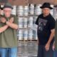 Dois dançarinos idosos posam em galpão com barris de cerveja ao fundo