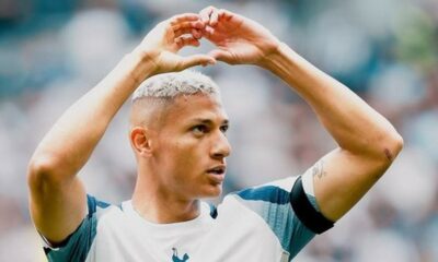 Richarlison com cabelo platinado faz gesto de coração com as mãos em campo de futebol
