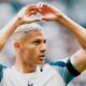 Richarlison com cabelo platinado faz gesto de coração com as mãos em campo de futebol